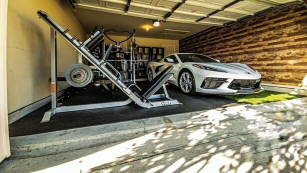 Un garage avec une voiture de sport blanche, un ascenseur et un mur en bois.