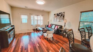 Un salon spacieux doté d’un parquet, d’un ensemble de canapés, d’une table basse et d’un téléviseur posé sur un meuble.