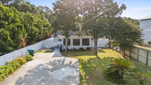 A residential backyard with a house, a concrete driveway, a wooden fence, and various trees. - Barefoot Beach House by PHG (Panama City Beach)