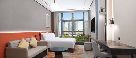 Habitación de hotel moderna con cama, sofá, mesa de comedor y un amplio ventanal con vistas a la ciudad.