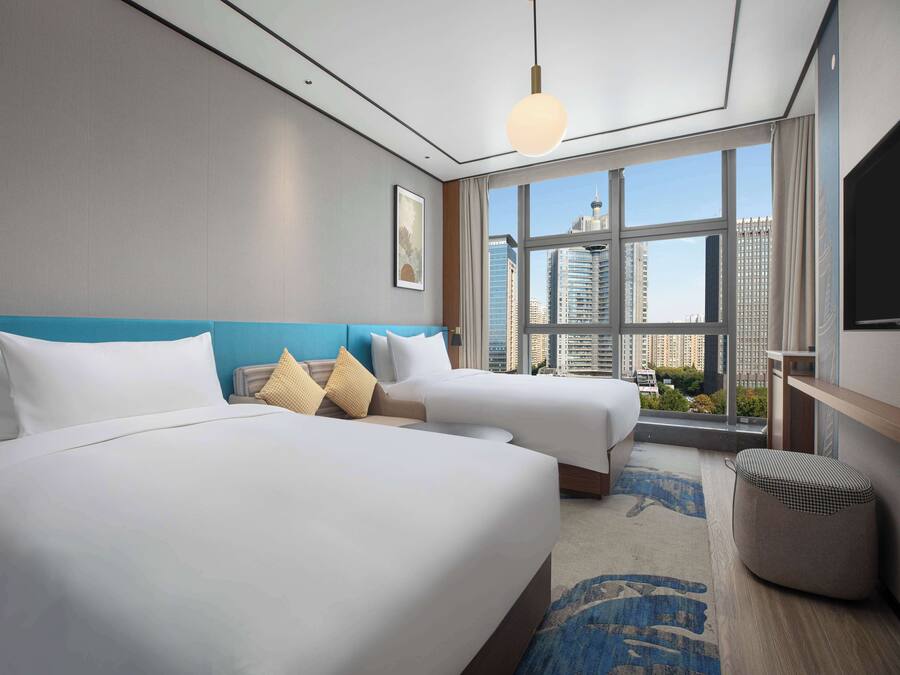 Quarto de hotel com duas camas, uma janela grande com vista para a cidade e design moderno.