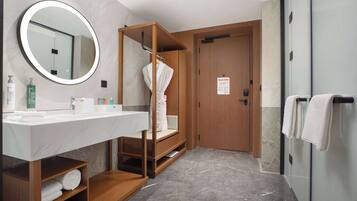 Un baño moderno con tocador de madera, un espejo redondo y una bata colgada en un perchero.