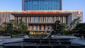A modern hotel with a prominent sign for Hilton Garden Inn, featuring a large glass facade and a well-maintained outdoor area with a water feature. - Hilton Garden Inn Luoyang Kaiyuan Avenue (Luoyang)