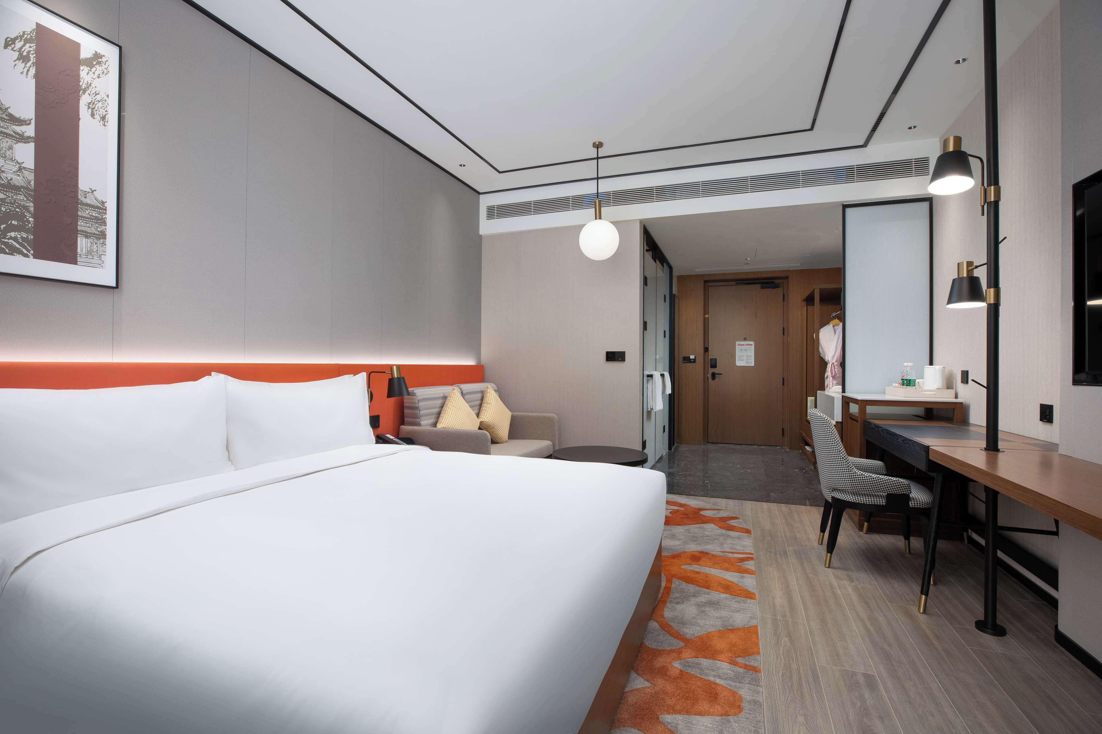 A hotel room with a large bed, a desk, a chair, a mirror, and a small table.