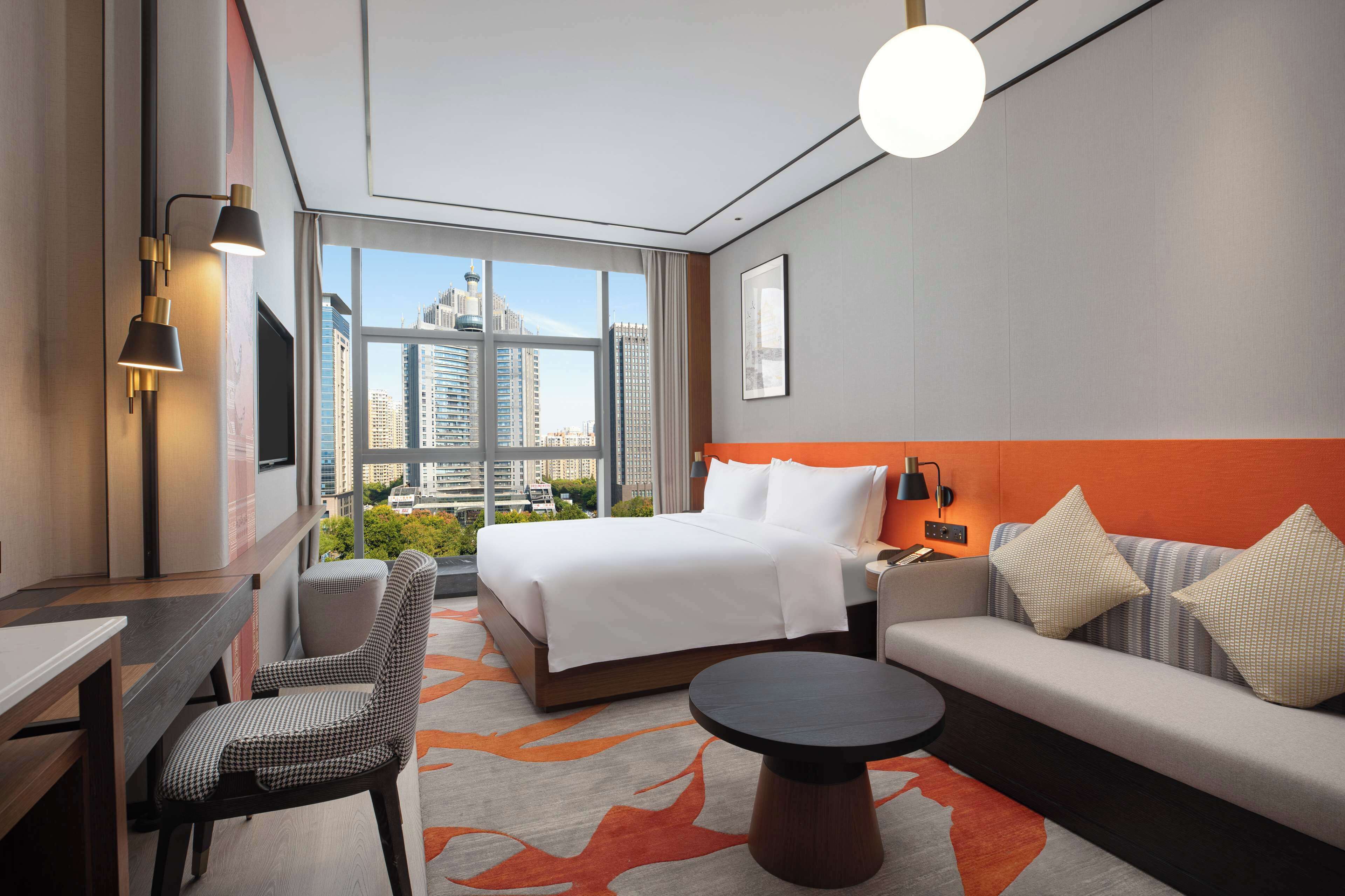 Una habitación de hotel moderna con una cama grande, un sofá, una mesa de comedor y vistas a la ciudad.