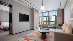 A modern hotel room with a large window, a flat-screen TV, a round coffee table, and a sofa with decorative pillows. - Hilton Garden Inn Luoyang Kaiyuan Avenue (Luoyang)