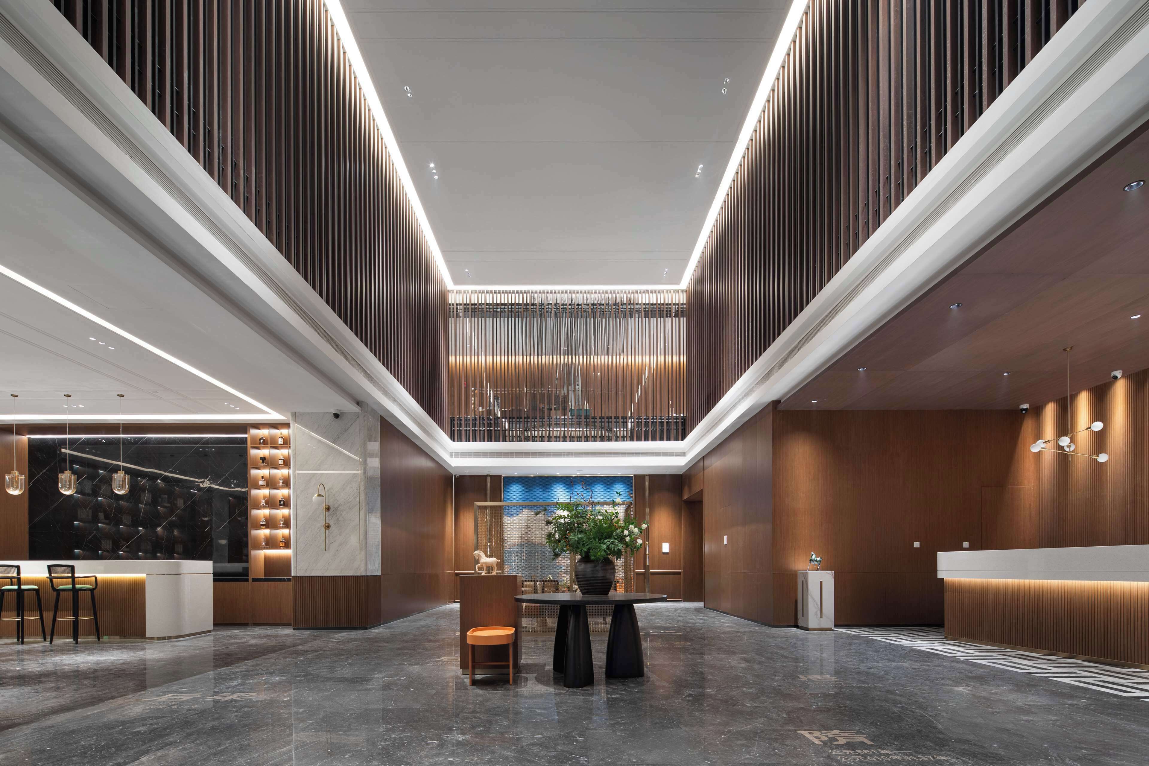 A modern hotel lobby with a reception desk, seating area, and a large potted plant.