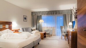 A hotel room with a large bed, two armchairs, a desk, and a view of the outdoors through sheer curtains. - Residence Mathilda in the Vinschgau apple orchard - Refined & simple (Schlanders)