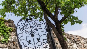 A wrought iron gate with intricate designs, set against a stone wall and a tree with green leaves. - Residence Mathilda in the Vinschgau apple orchard - Refined & simple (Schlanders)