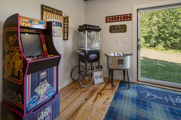Una habitación con una máquina de videojuegos retro, una máquina de palomitas y un cartel de cine.