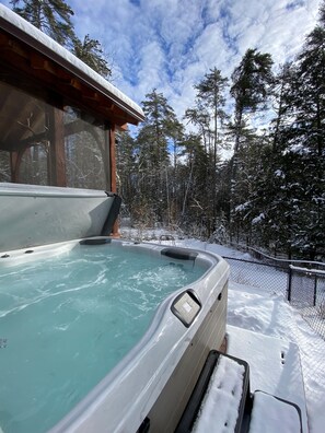 A hot tub surrounded by snow-covered trees and a wooden cabin. - Bolton Bear House|Dock Slip|Hot Tub|12 Beds|Pet Friendly| (Bolton Landing)