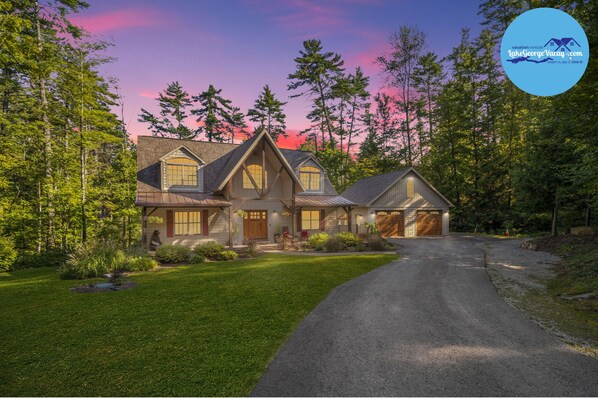 A large, two-story house with a steeply pitched roof, multiple chimneys, and a well-maintained lawn. - Bolton Bear House|Dock Slip|Hot Tub|12 Beds|Pet Friendly| (Bolton Landing)