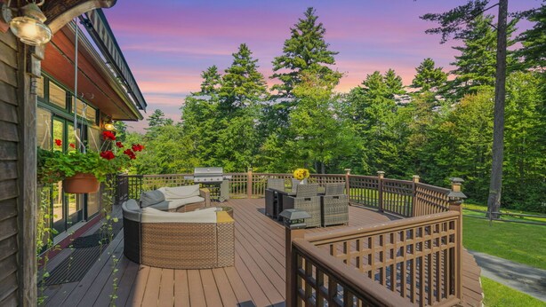 Una terraza de madera con mobiliario exterior, una parrilla y vistas a un área boscosa.