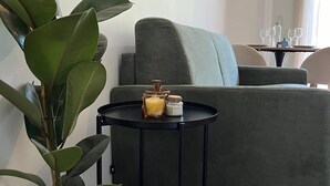 Un salon moderne avec un canapé vert, une petite table ronde noire sur laquelle se trouvent une bougie et un vase, et une grande plante en pot.