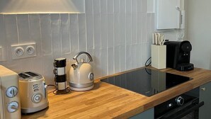 Une cuisine moderne avec un plan de travail en bois, une bouilloire, un grille-pain, une machine à café et un téléviseur fixé au-dessus du plan de travail.