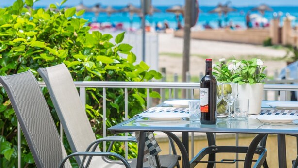 Una mesa con una botella de vino, copas y un menú en un balcón con vista a la playa.