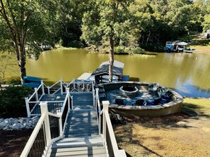 A wooden dock leading to a docked boat, a fire pit, and a grassy area with chairs. - 7 Bedrooms-4 Kings, 7 Baths! Sleeps 20! Pool Table, Ping Pong & many water toys! (Bracey)