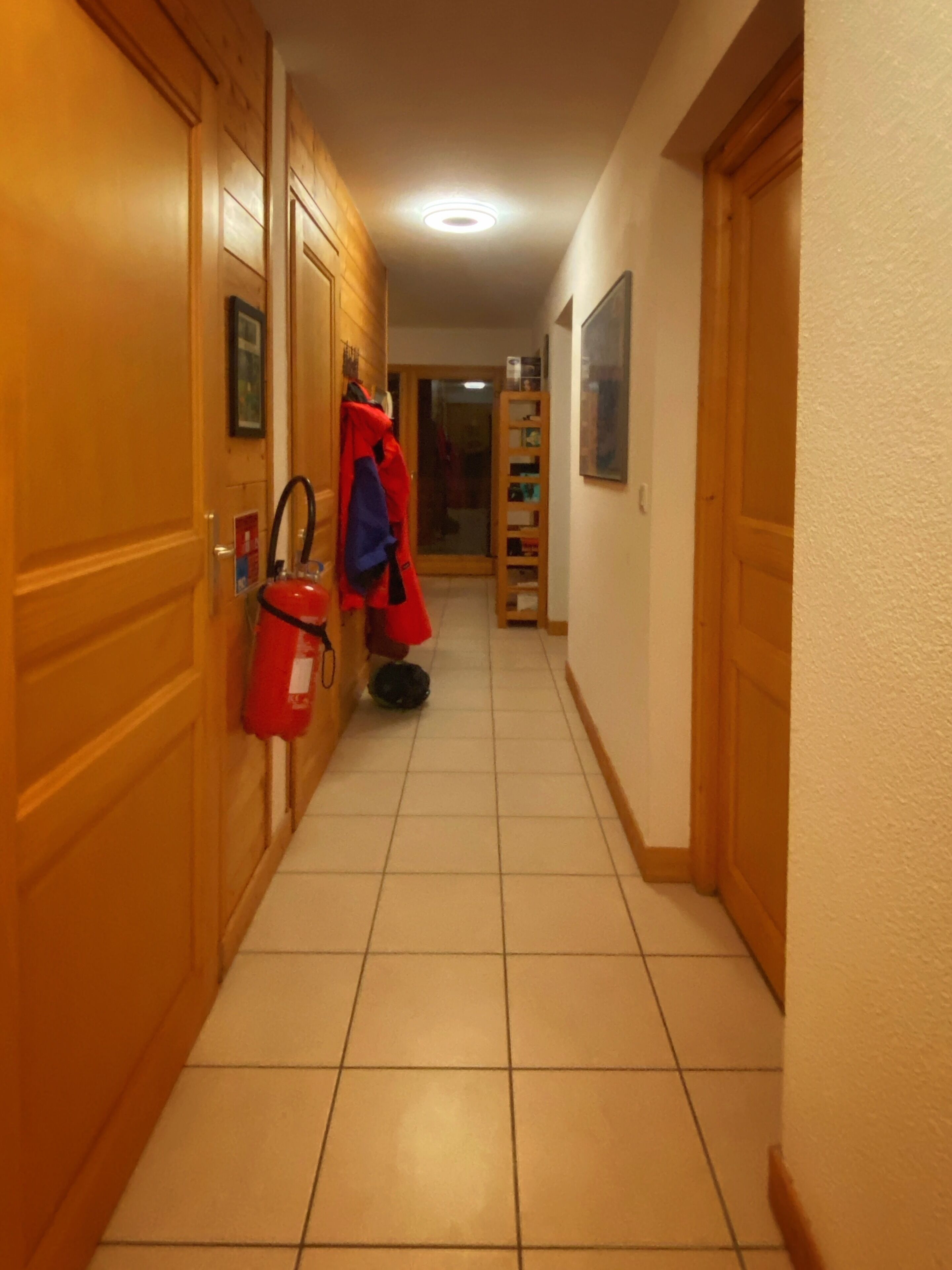 Un corridoio con porte in legno, un estintore rosso e un appendiabiti con cappotto rosso e blu.