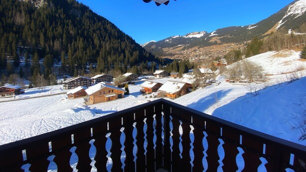 Ein verschneites Dorf mit Holzhäusern und einer Bergkulisse.