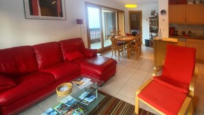 Ein Wohnzimmer mit einem roten Sofa, einem Glastisch mit Zeitschriften, einem roten Sessel und einem Streifenmuster-Teppich.