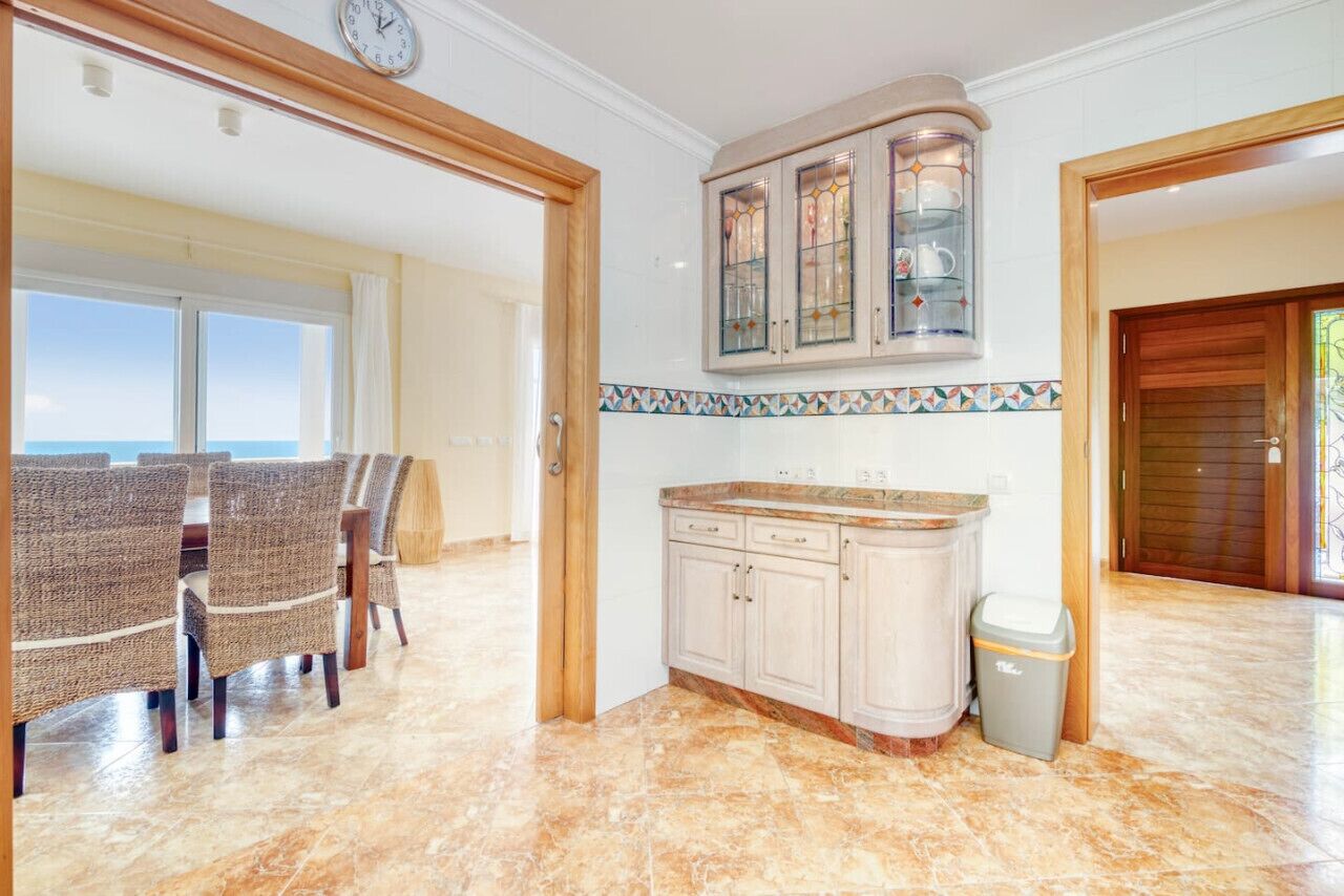 A kitchen with a marble floor, white cabinets, and a glass cabinet with dishes.
