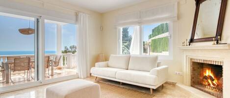 A spacious living room with a white sofa, a fireplace, and a balcony with outdoor furniture.