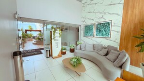 A modern living room with a curved sofa, a coffee table, and potted plants. - Branco Haus Seaview By Living (João Pessoa)
