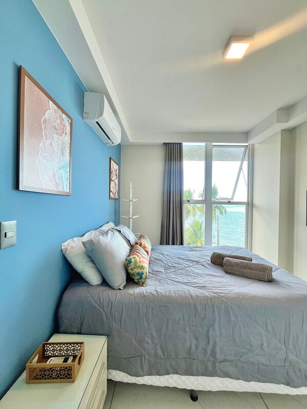 Une chambre à coucher avec un lit, une table de chevet, une fenêtre avec des rideaux et une vue sur la mer.