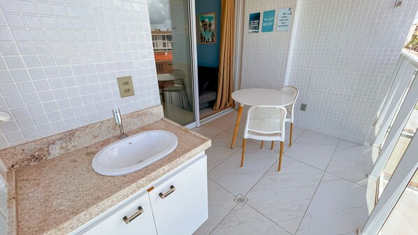 Une salle de bain avec un lavabo, un miroir et une petite table accompagnée d’une chaise.