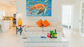 A living room with a sofa, coffee table, and artwork of a sea turtle. - Three Bedroom Superior Apartment (Jolly Harbour)