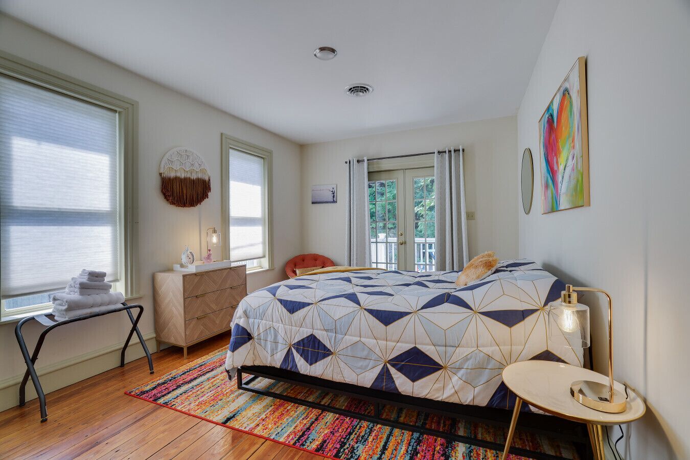 Une chambre à coucher avec un lit, un bureau, une chaise, une fenêtre avec des rideaux et un tapis coloré.