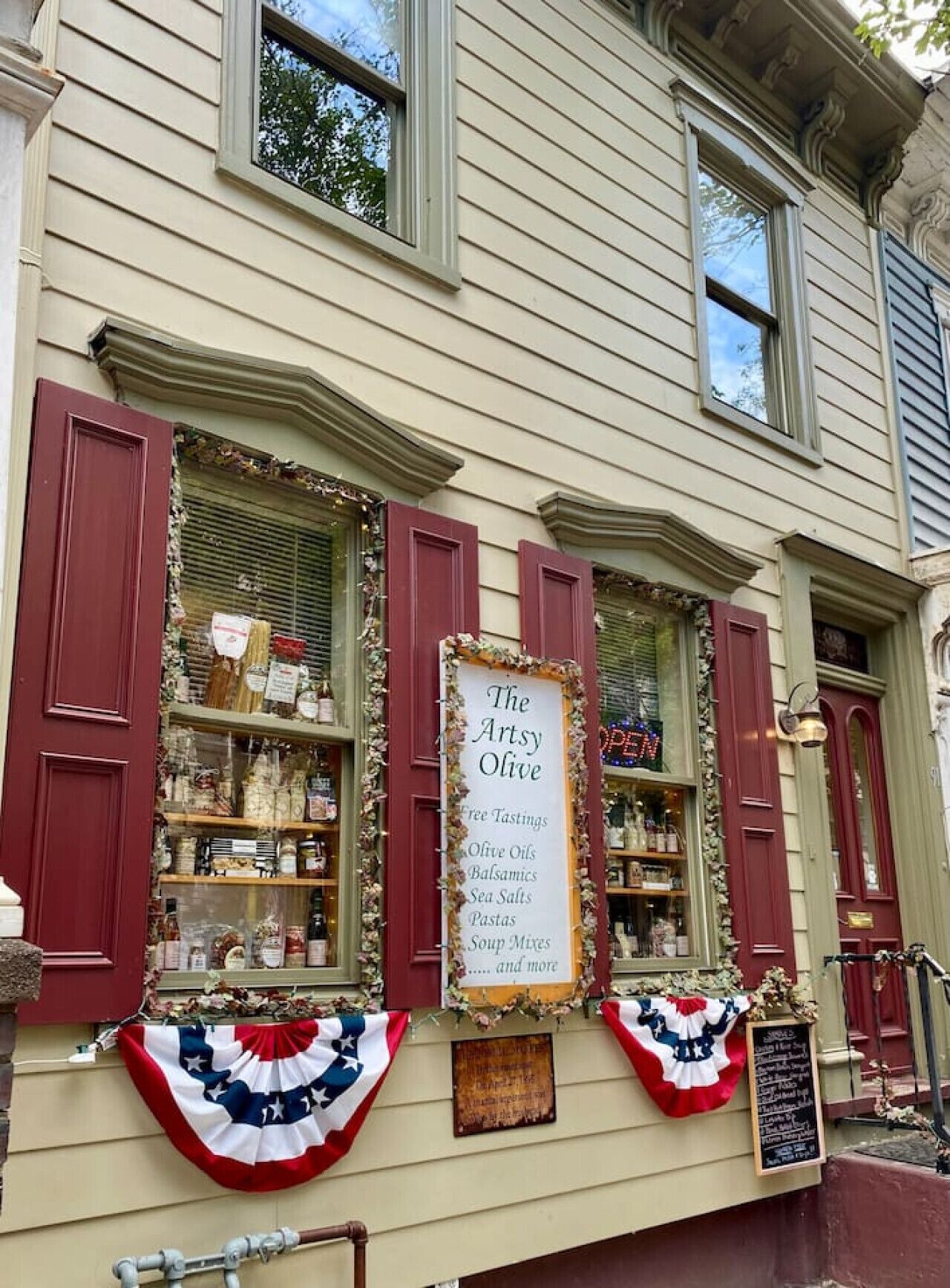 A storefront with a sign advertising 'The Artsy Olive' offering free tastings, olive oils, balsamics, sea salts, pastas, and soup mixes.
