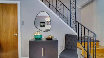 Een trap met een zwarte metalen leuning, een donkergrijze fauteuil, een houten deur en een kast met een turquoise vaas.
