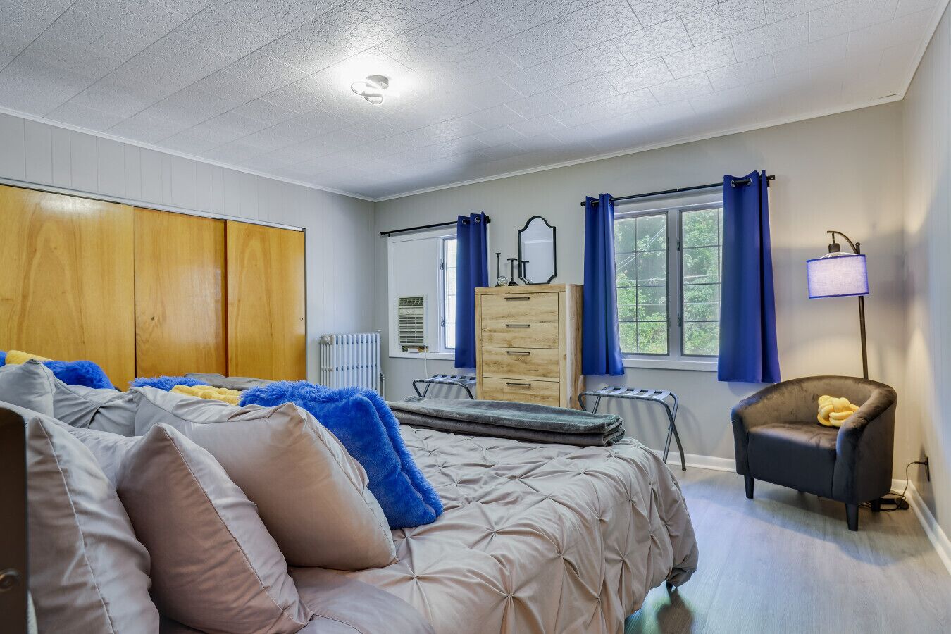 A bedroom with a bed, a dresser, a chair, and a window with curtains.