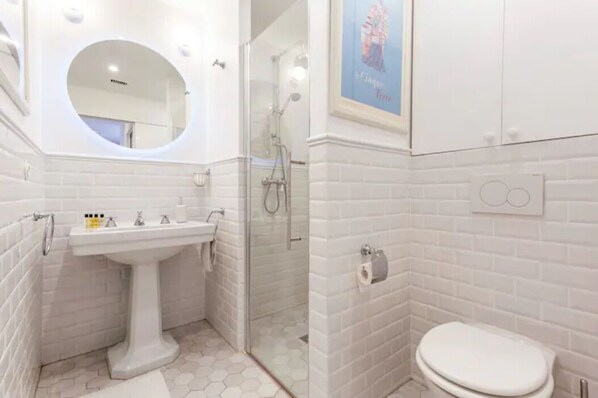 Un baño con lavamanos, espejo, inodoro y ducha.