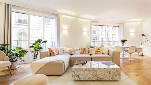 A modern living room with a sectional sofa, a marble coffee table, and large windows offering a view of the city.