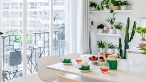 A bright room with a dining table set for tea, surrounded by potted plants and a view of a balcony with outdoor furniture.