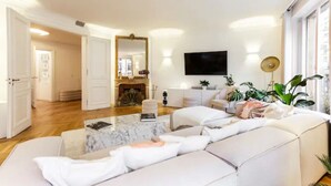 A spacious living room with a large sofa set, a coffee table, and a flat-screen TV mounted on the wall.