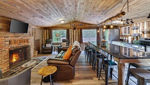 A cozy cabin interior with a fireplace, leather sofa, bar area, and a television mounted on the wall. - Cozy Log Cabin in Jim Thorpe (Jim Thorpe)