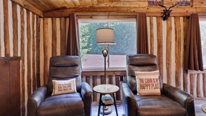 A cabin interior with wooden walls, two leather chairs with cushions, a small round table, and a lamp. - Cozy Log Cabin in Jim Thorpe (Jim Thorpe)