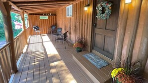 A wooden porch with a covered area, two chairs, a small table, and a door with a wreath. - Cozy Log Cabin in Jim Thorpe (Jim Thorpe)