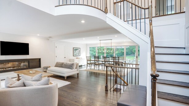 A spacious living area with a fireplace, a dining table with chairs, and a staircase with a railing. - Expansive Modern Sag Harbor Home with Private Heated Pool, Perfect for Families (Sag Harbor)