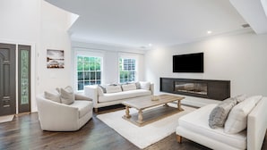 A modern living room with a fireplace, white sofas, and a flat-screen TV. - Expansive Modern Sag Harbor Home with Private Heated Pool, Perfect for Families (Sag Harbor)