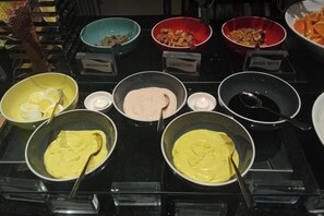Un buffet proposant divers plats présentés dans des récipients étiquetés, notamment des œufs, des champignons, des croûtons et une sauce.