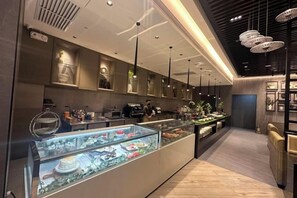 Un intérieur moderne avec un long comptoir où sont exposés divers produits alimentaires, un éclairage suspendu et un design épuré et minimaliste.