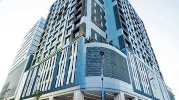 Un moderno edificio de gran altura con fachada de esquina curva, varios balcones y una entrada destacada con una cubierta de vidrio.