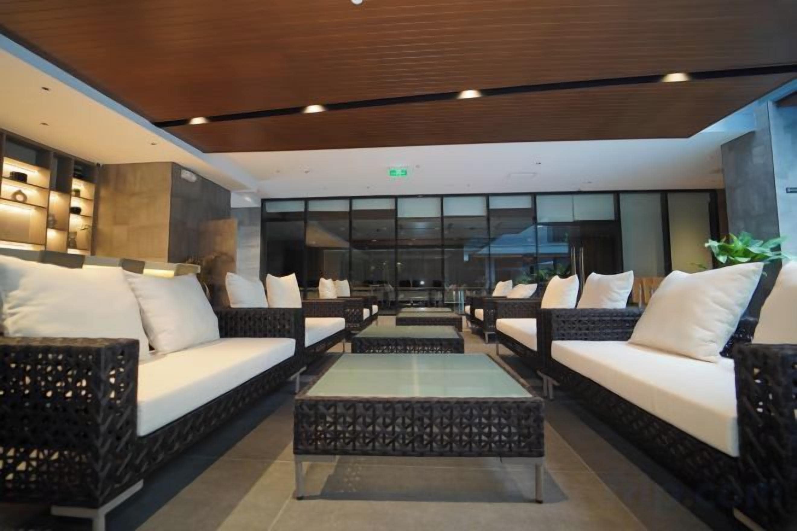 A modern lobby with wicker sofas, a glass coffee table, and a wooden ceiling.