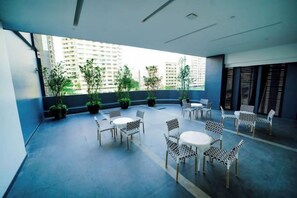 Un espace extérieur aménagé avec des tables et des chaises, des plantes en pot et une vue sur les bâtiments.