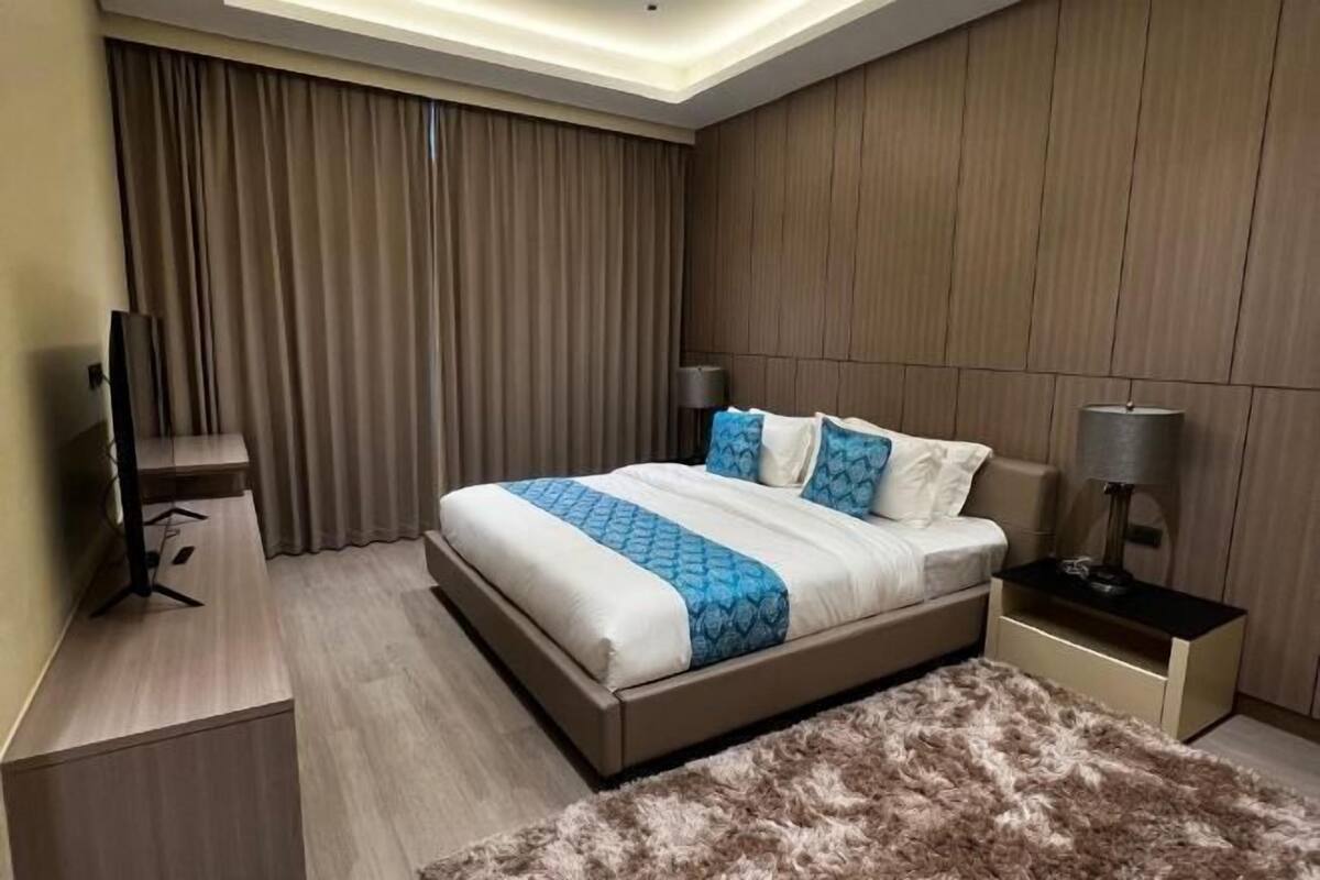 Ein modernes Hotelzimmer mit Bett, Vorhängen, einem Flachbildfernseher, einem Schreibtisch und einer Lampe.