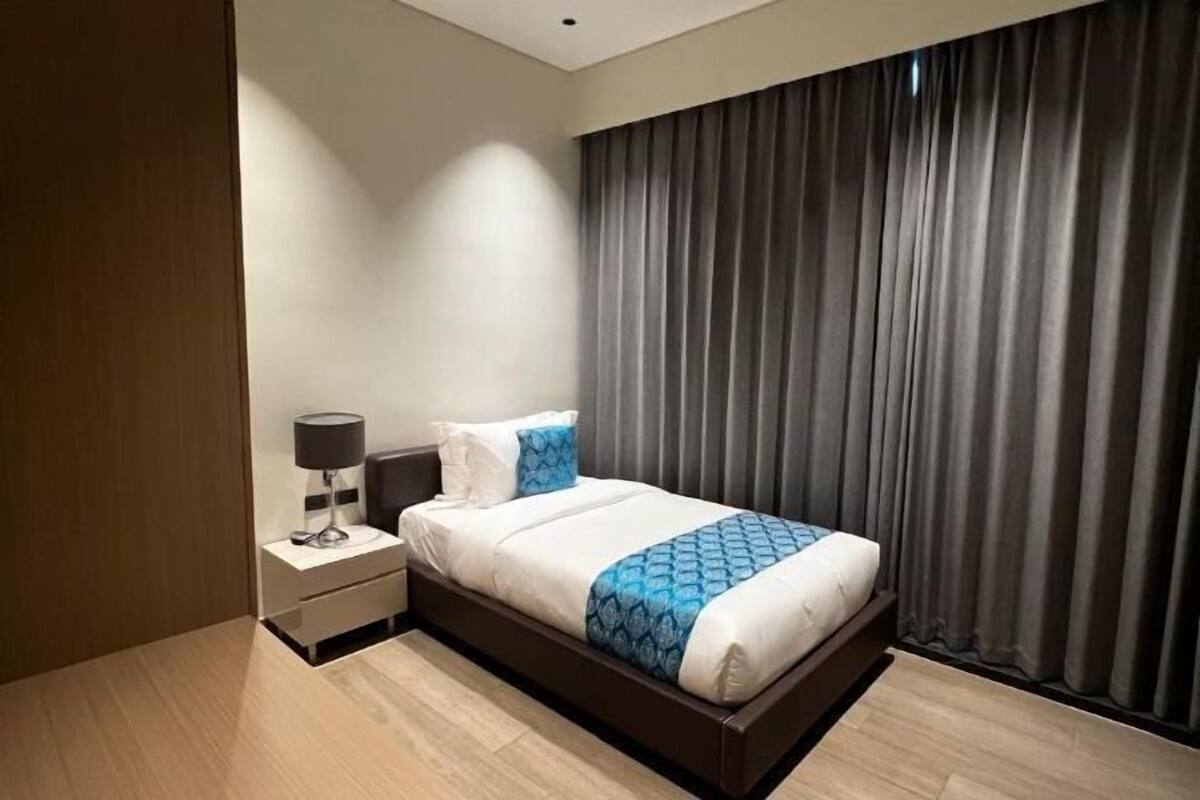 Ein modernes Hotelzimmer mit Bett, Nachttisch, Lampe und Vorhängen.